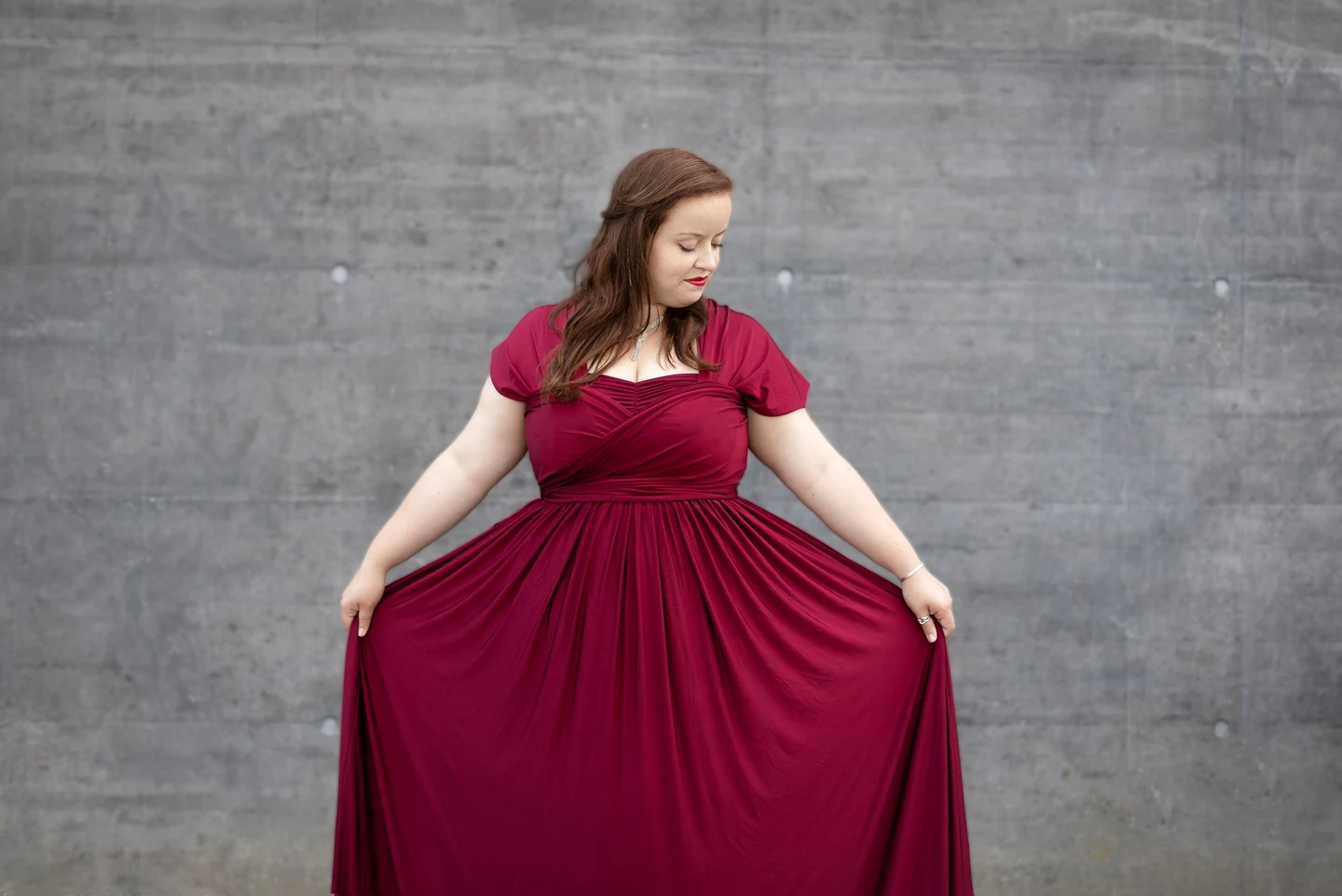 Portrait en pied de Donata Meyer-Kranixfeld en robe bordeaux devant un mur de béton
